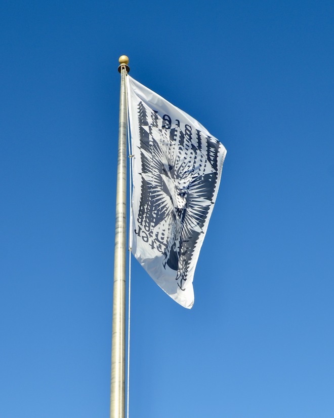 A white and black graphic design on a flag flying against a clear blue sky